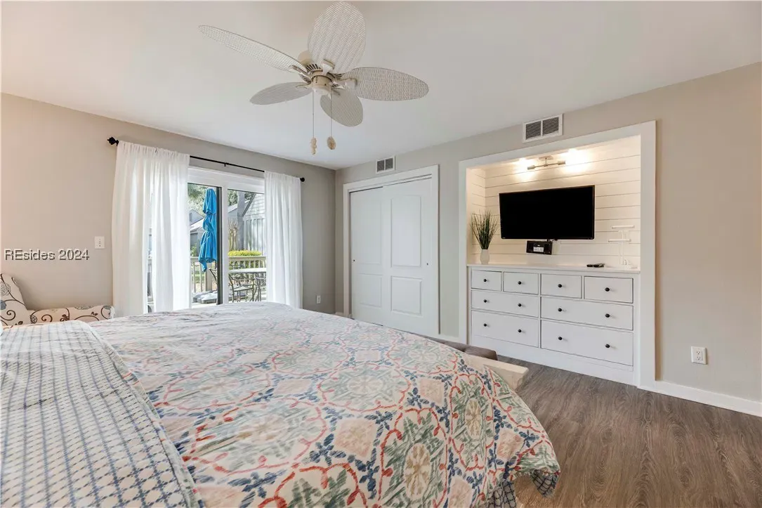 Bedroom with patterned bedspread, built-in dresser, mounted TV, and sliding glass door