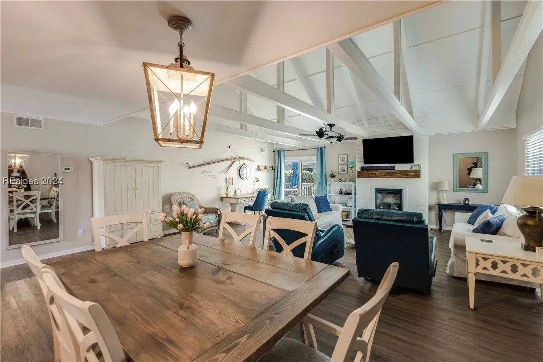 Open dining and living area with vaulted beamed ceiling, wooden table, fireplace, and blue seating