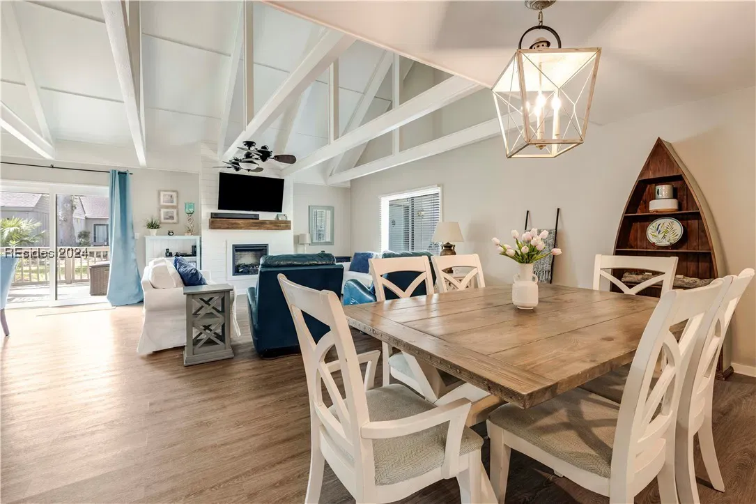 Open dining and living area with vaulted beamed ceiling, wood table, and fireplace beyond