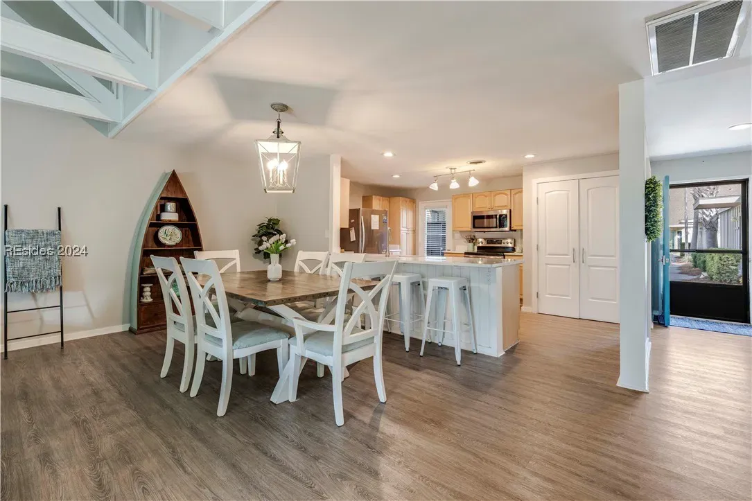 Open dining area with wood table, white chairs, pendant light, and kitchen beyond