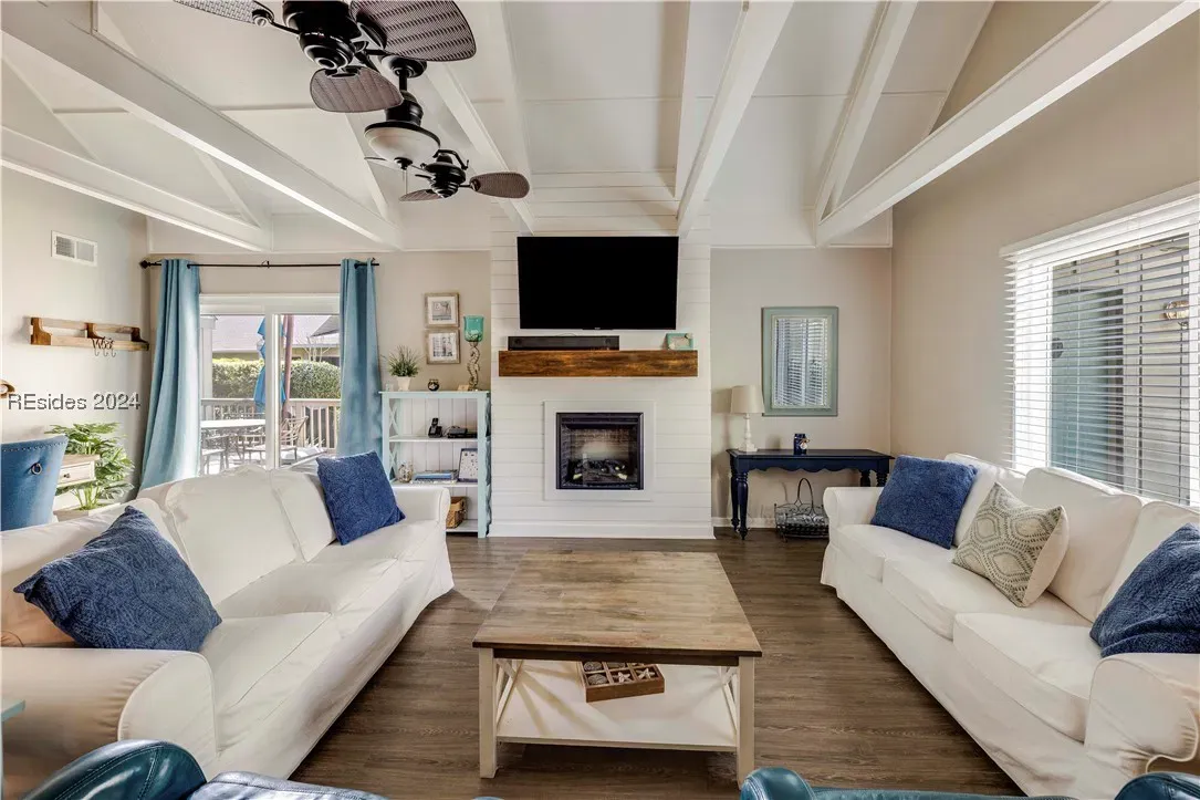 Living room with vaulted beamed ceiling, fireplace, mounted TV, and two white sofas