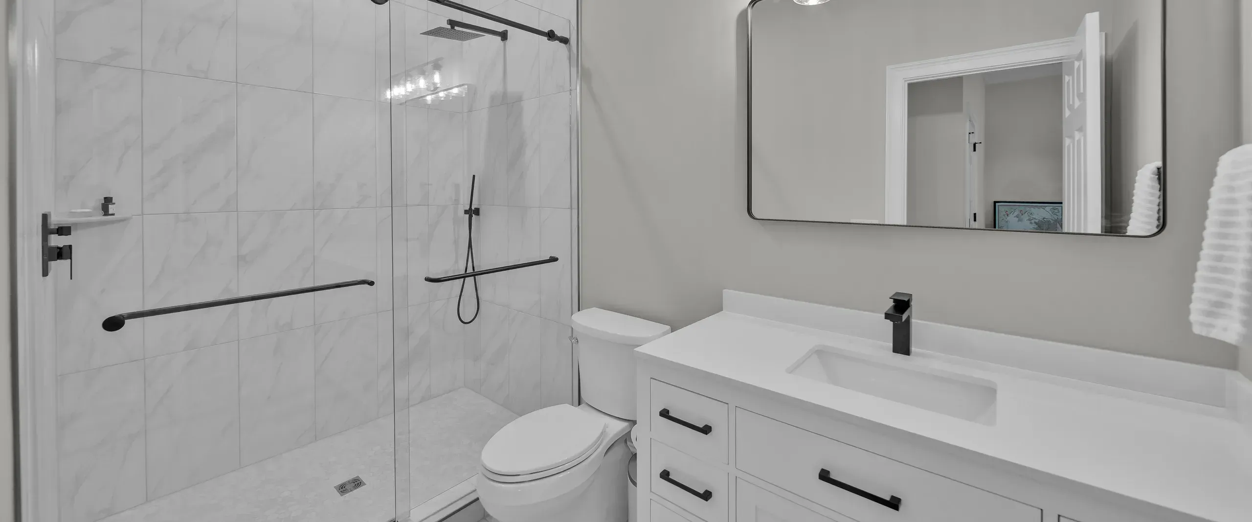 A remodeled bathroom features a marble-tiled walk-in shower with a black barn-door style glass enclosure and rainfall showerhead beside a white vanity with a rectangular sink and framed mirror.