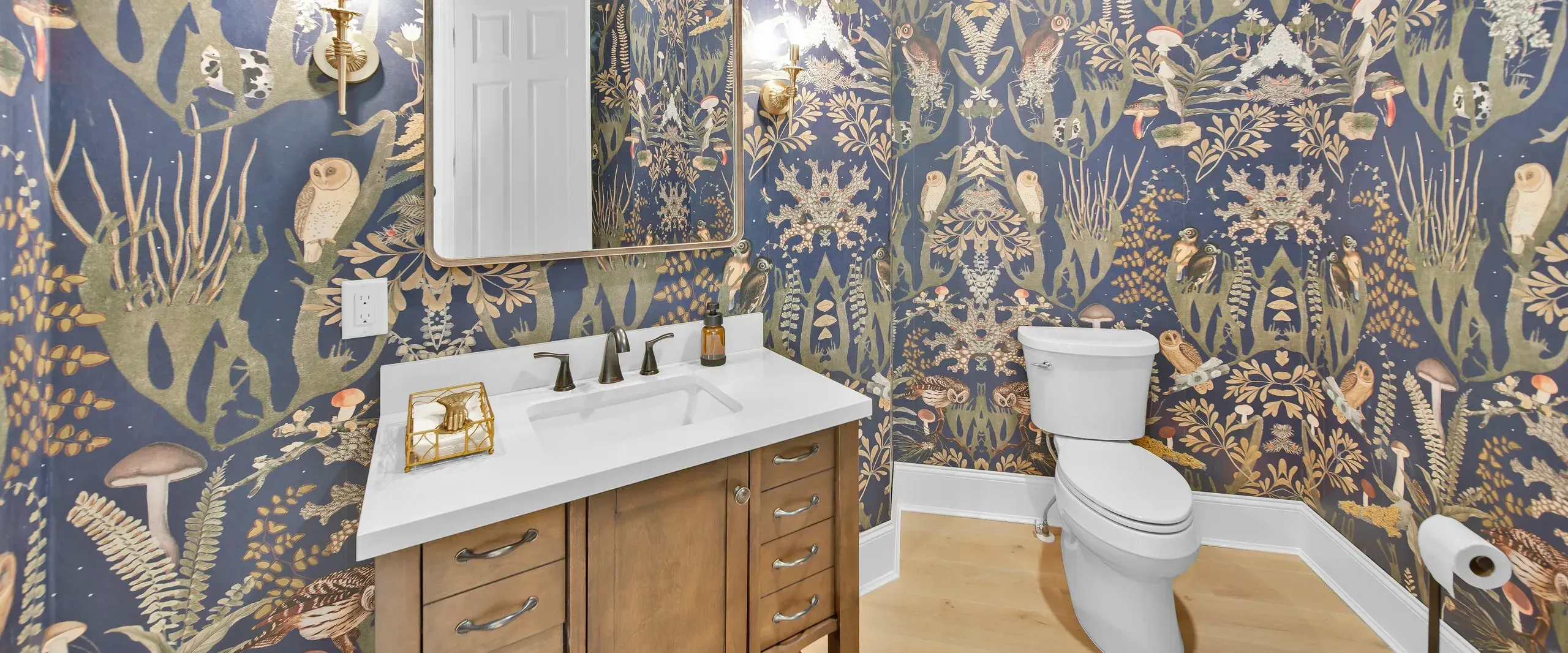 Powder room with owl-patterned wallpaper, wood vanity, white countertop, and toilet