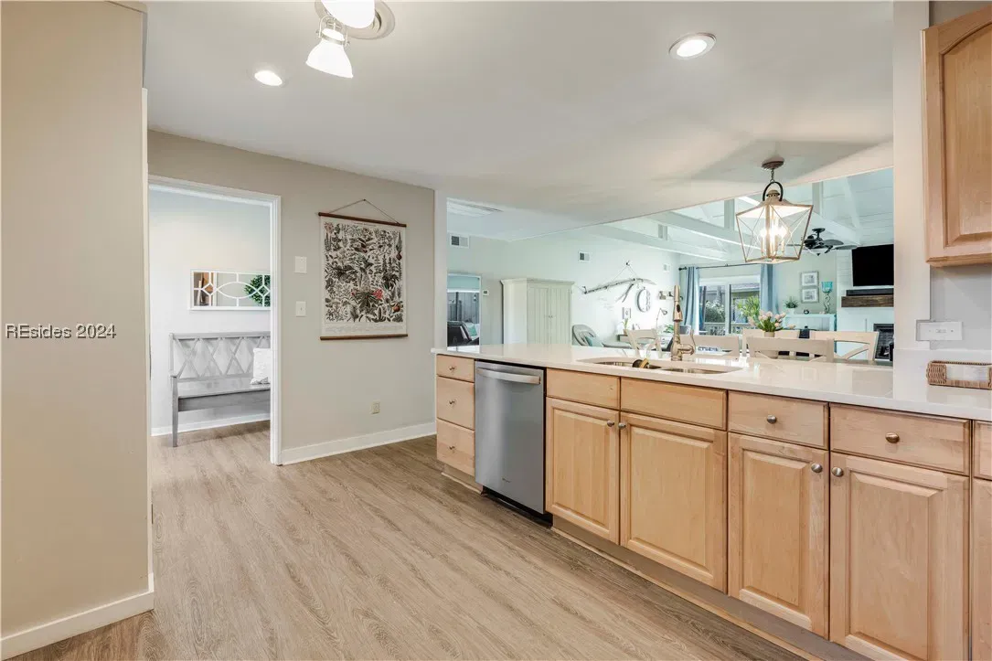 Kitchen with light wood cabinets, dishwasher, sink, and view into open living area