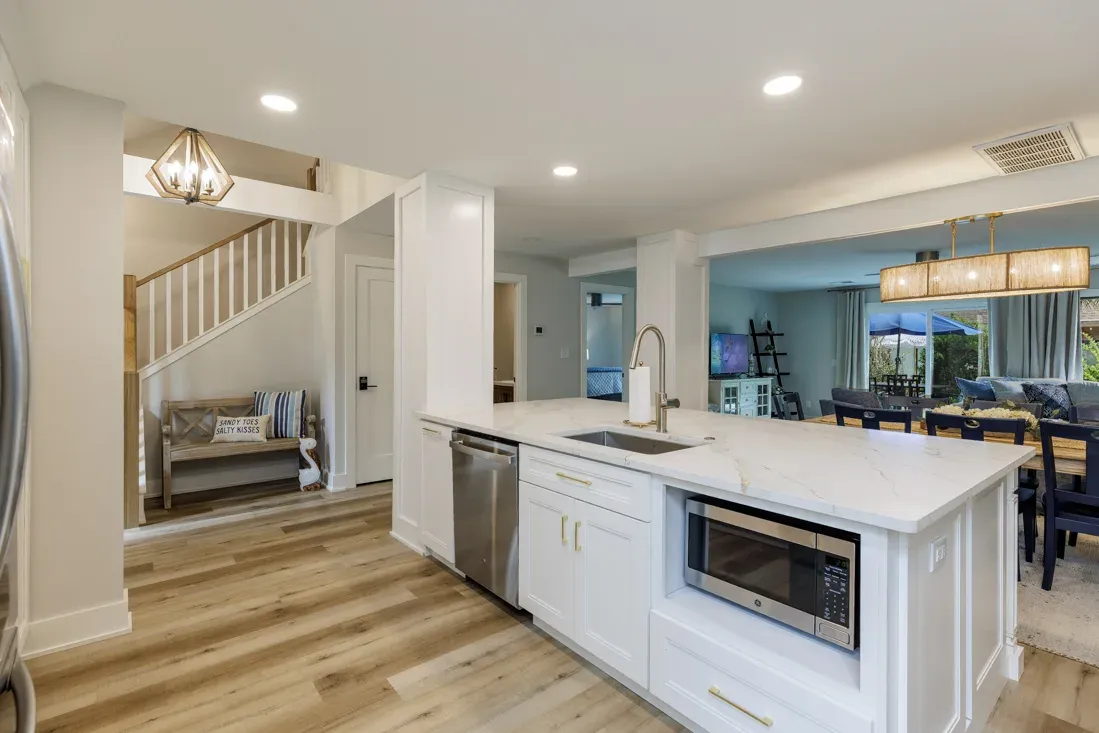 Open kitchen island with white countertop, sink, microwave, overlooking staircase and dining area