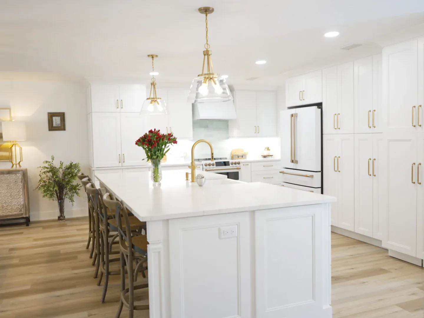 Kitchen with white cabinets, large island with seating, gold pendant lights, and white refrigerator