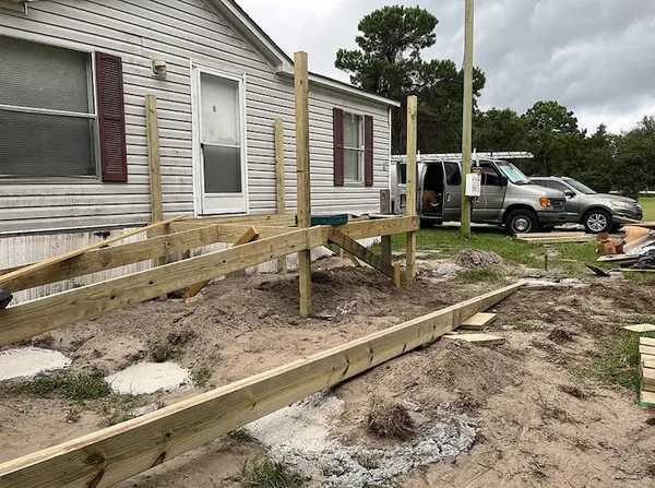Wooden deck framing under construction beside house, with work van parked nearby