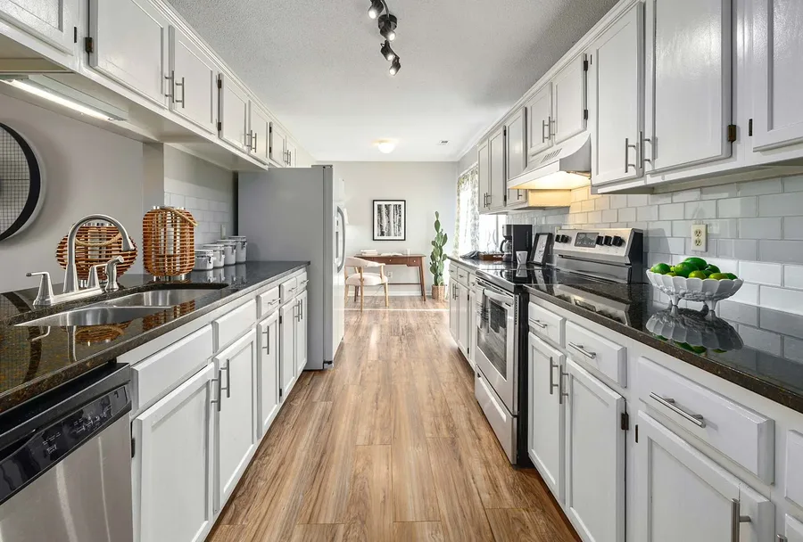 Galley kitchen with white cabinets, dark countertops, subway tile backsplash, and wood flooring