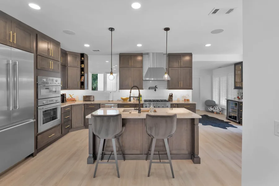 Kitchen with dark wood cabinets, island with sink and two gray stools, stainless appliances