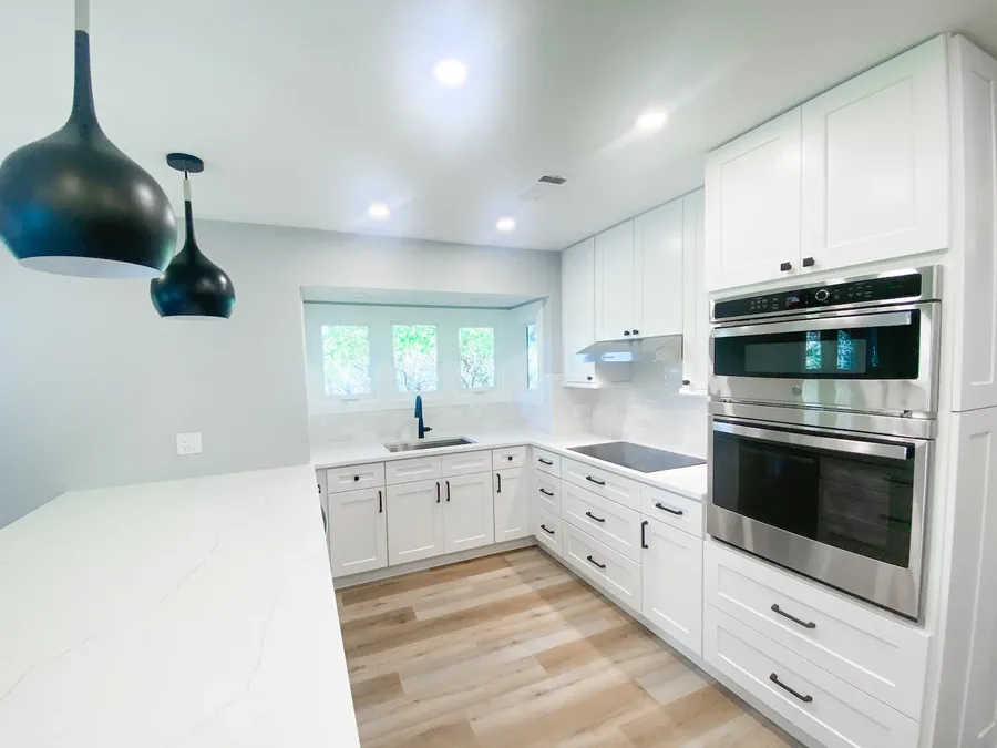 Kitchen with white cabinets, double wall ovens, cooktop, and window above the sink