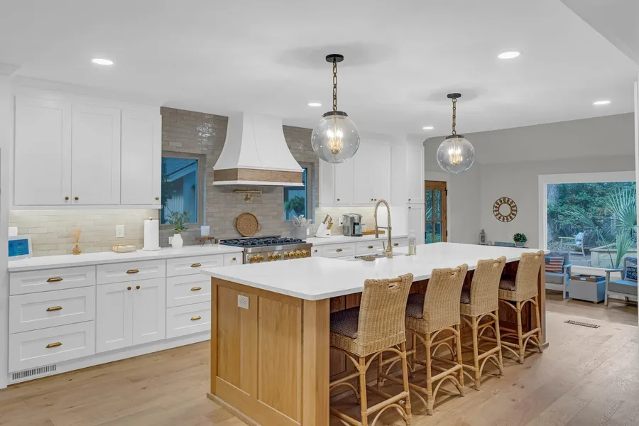 Kitchen with white cabinets, wood-toned island, woven stools, pendant lights, and gas range