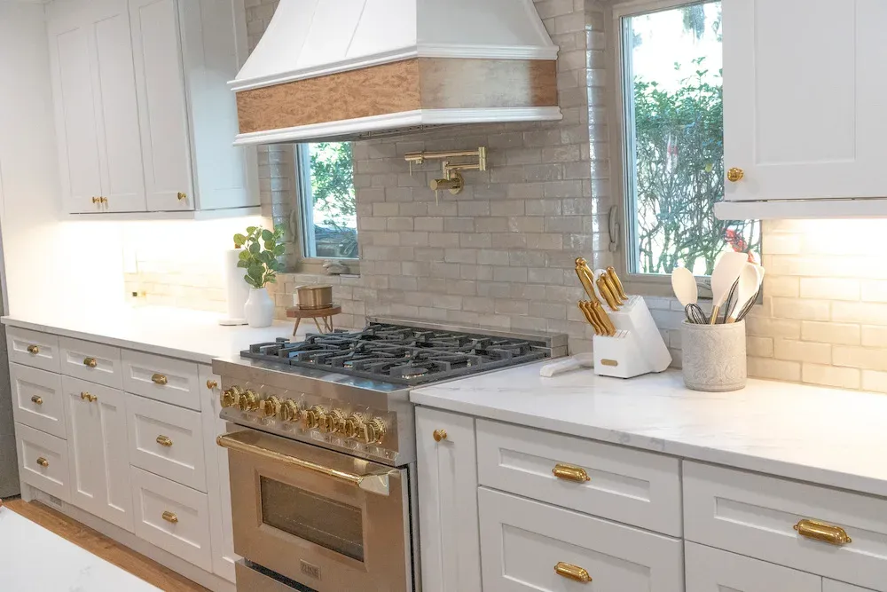 Kitchen with white cabinets, gold hardware, range hood, and subway tile backsplash