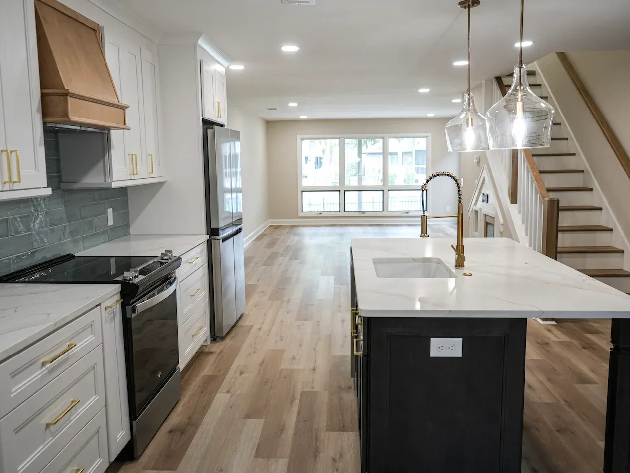 Kitchen with white cabinets, dark island with sink, pendant lights, and staircase nearby