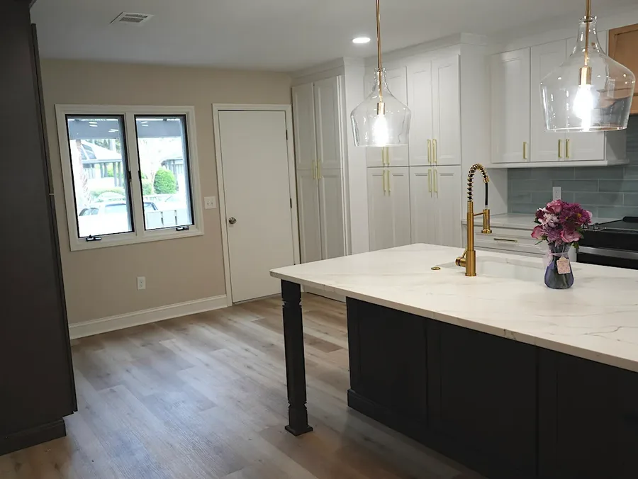 Kitchen with dark island, white countertop, gold faucet, and glass pendant lights