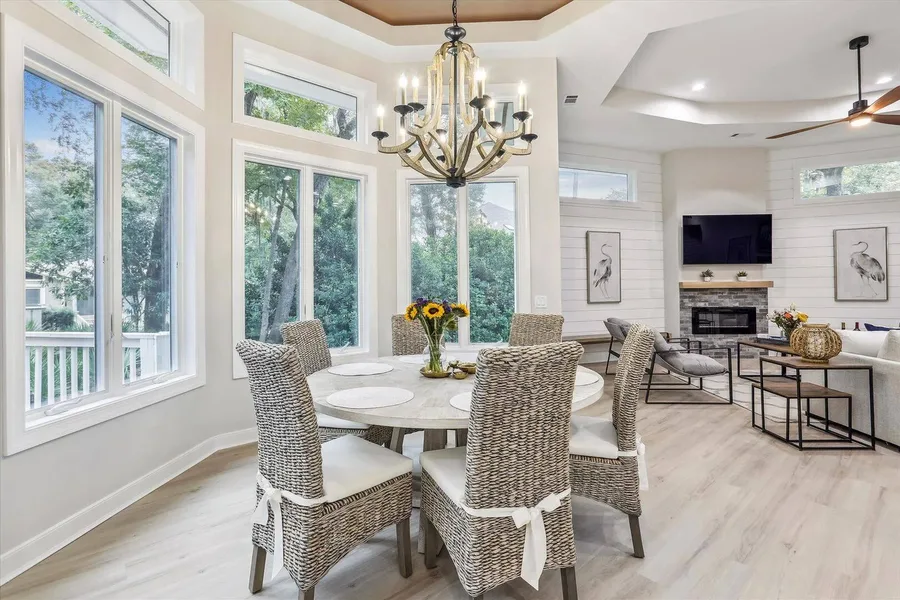 Dining area with woven chairs, round table, chandelier, and view into living room with fireplace