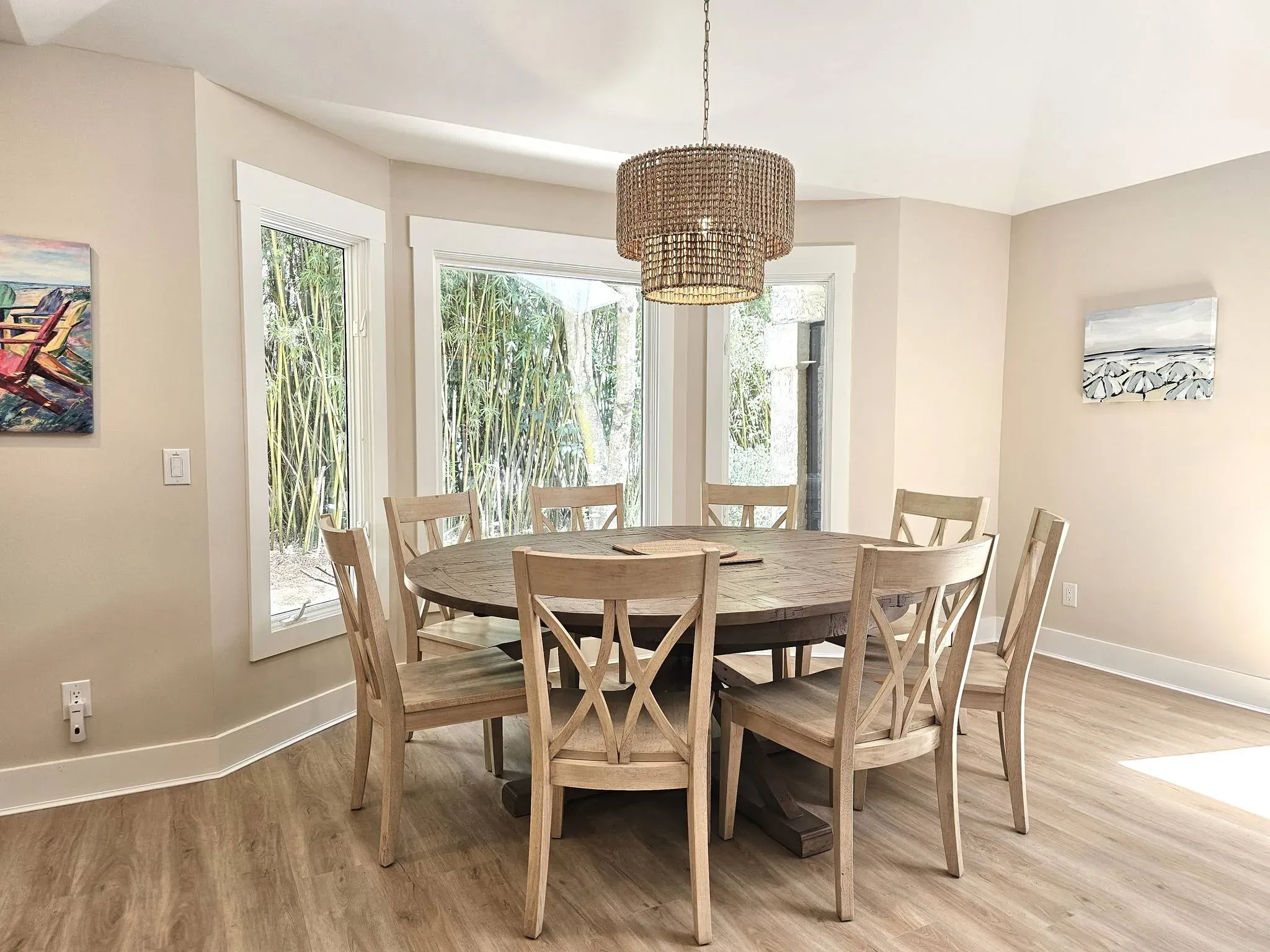 Dining room with a round wood table and chairs, a beaded chandelier, and bay windows