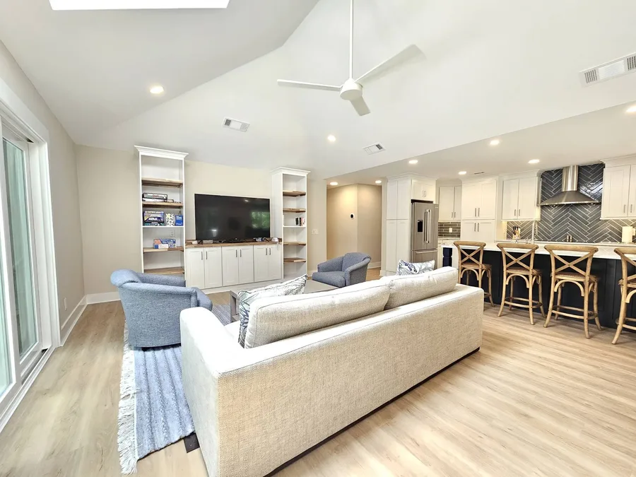 Open living room with a sofa, built-ins around the TV, and kitchen island seating beyond