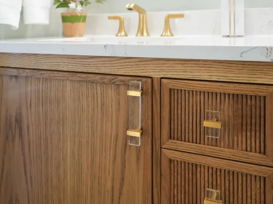 Close-up of wood vanity cabinet with gold hardware and white countertop sink