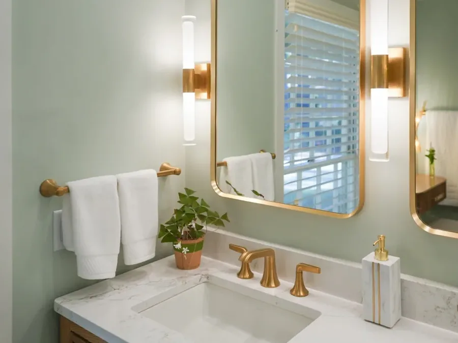 Bathroom vanity with gold faucet, framed mirror, sage walls, and white towels