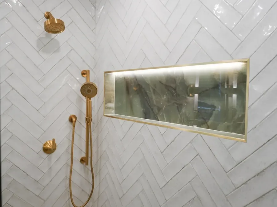 Shower with herringbone tile, gold fixtures, and lit recessed niche shelf