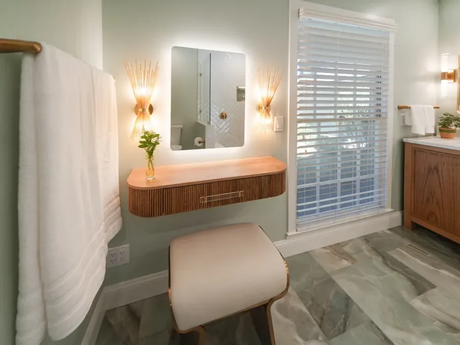 Bathroom vanity nook with backlit mirror, sconces, wood shelf, and cushioned stool