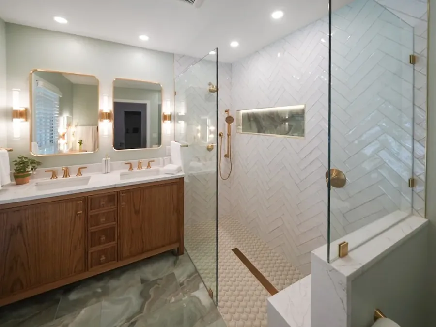 Bathroom with wood double vanity, two mirrors, and glass-enclosed herringbone tile shower