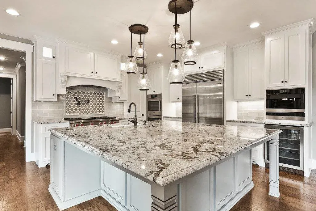 Kitchen with large granite island, white cabinets, pendant lights, and stainless steel appliances