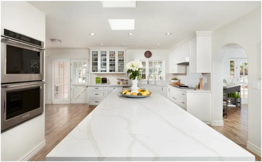 Kitchen with white cabinets, marble-topped island, built-in ovens, and arched doorway