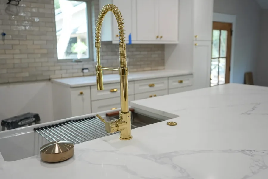 Kitchen island with a gold spring faucet, an undermount sink with a roll-up drying rack, and a white marble-look countertop