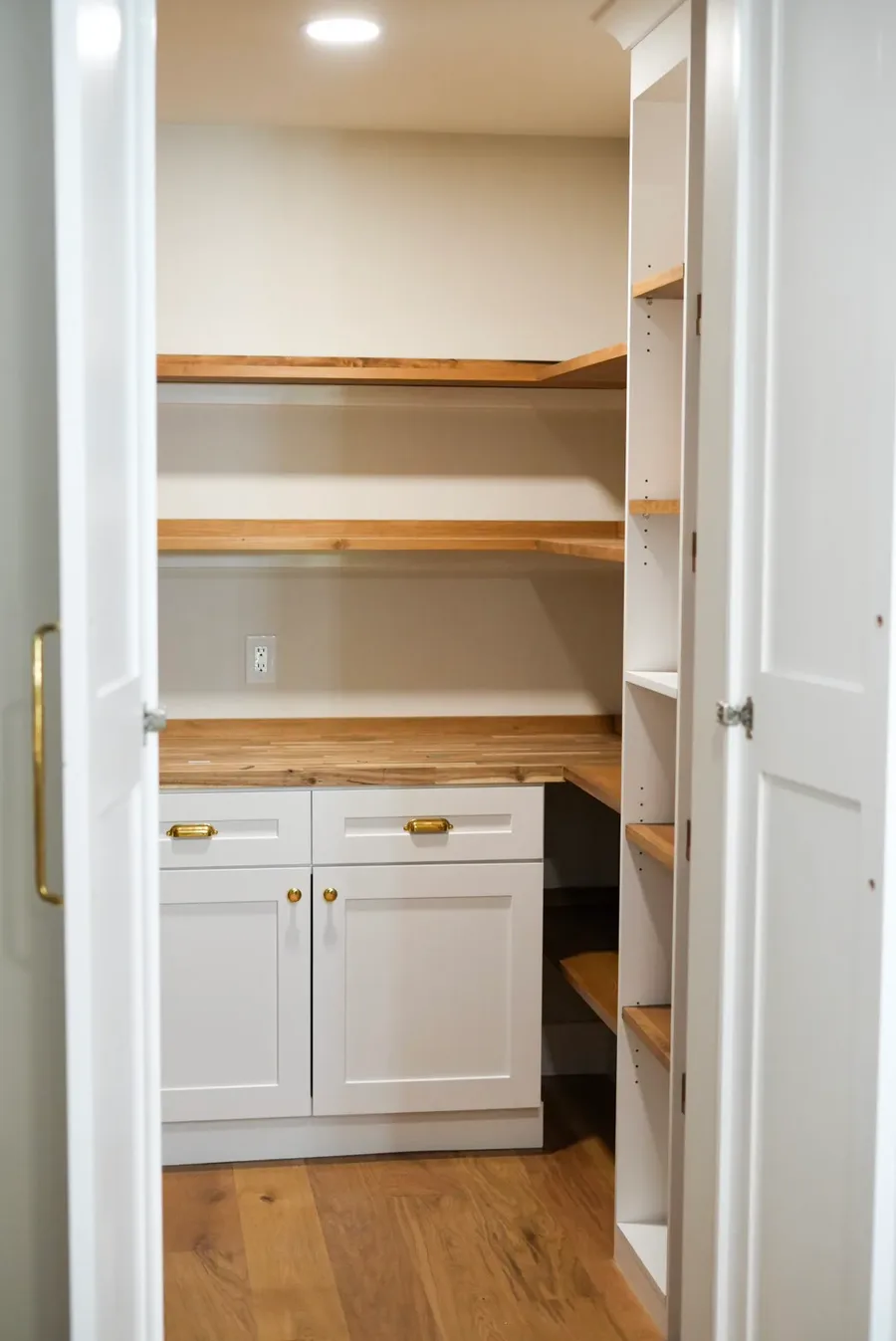 Pantry closet with white cabinets, wood shelving, butcher block counter, and brass hardware