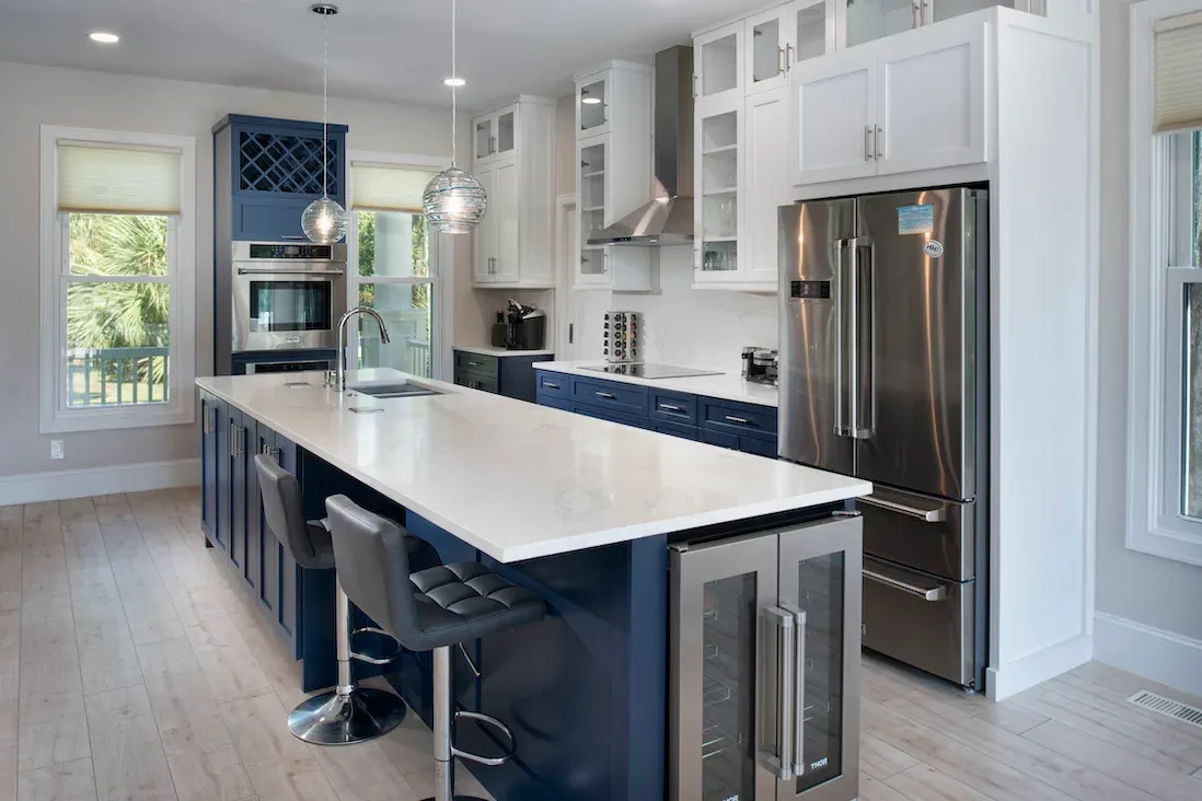 Kitchen with navy cabinets, white countertops, stainless appliances, and a long island with bar stools
