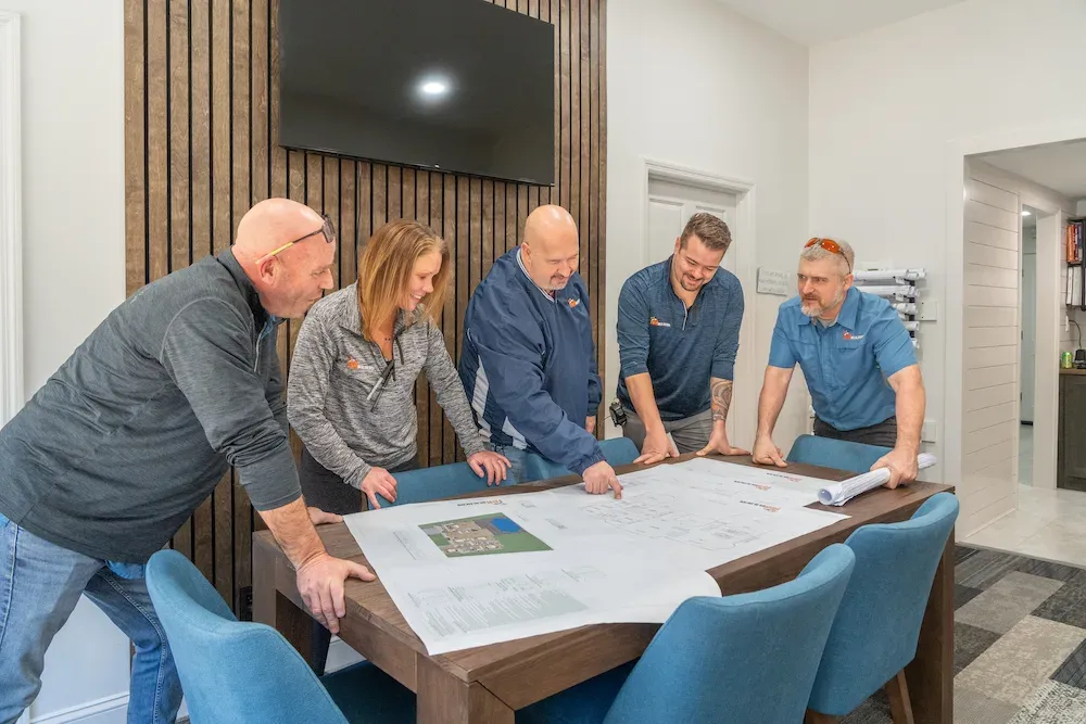 Five people reviewing building plans spread on a conference table together
