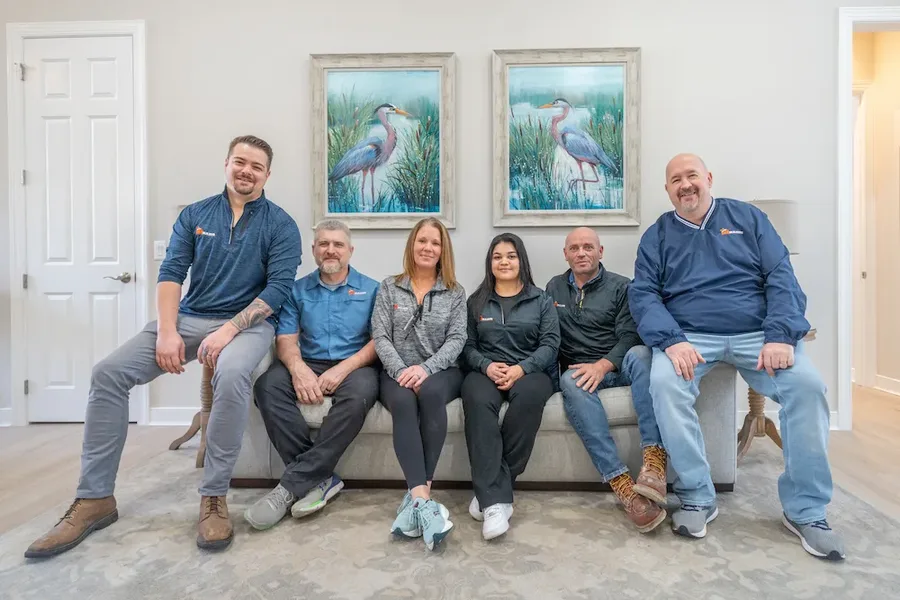 Six people on a gray sofa, bird artwork on wall behind them