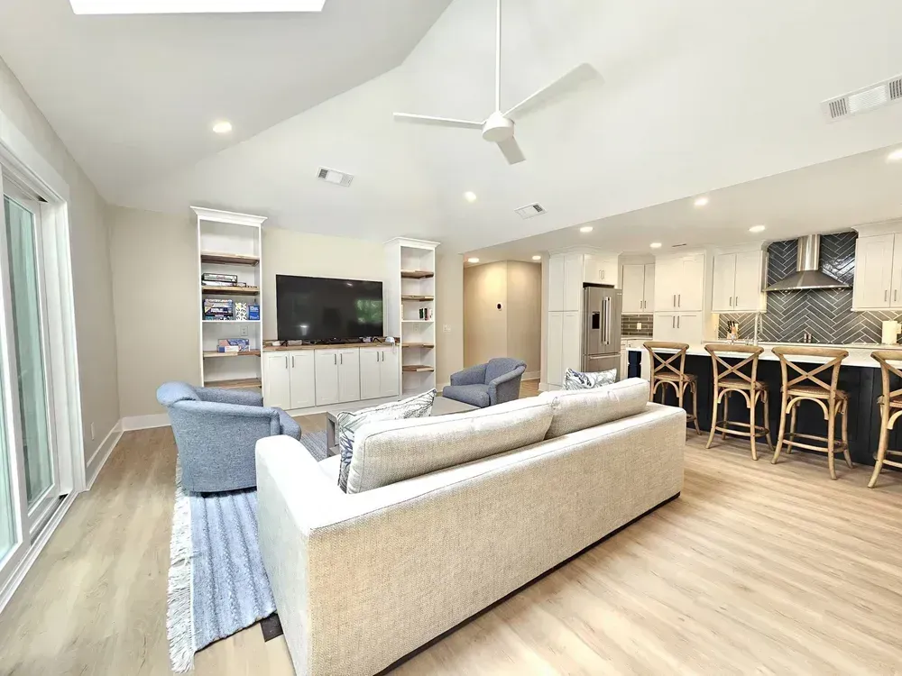Open living room with sofa, armchairs, TV, and adjoining kitchen island with barstools
