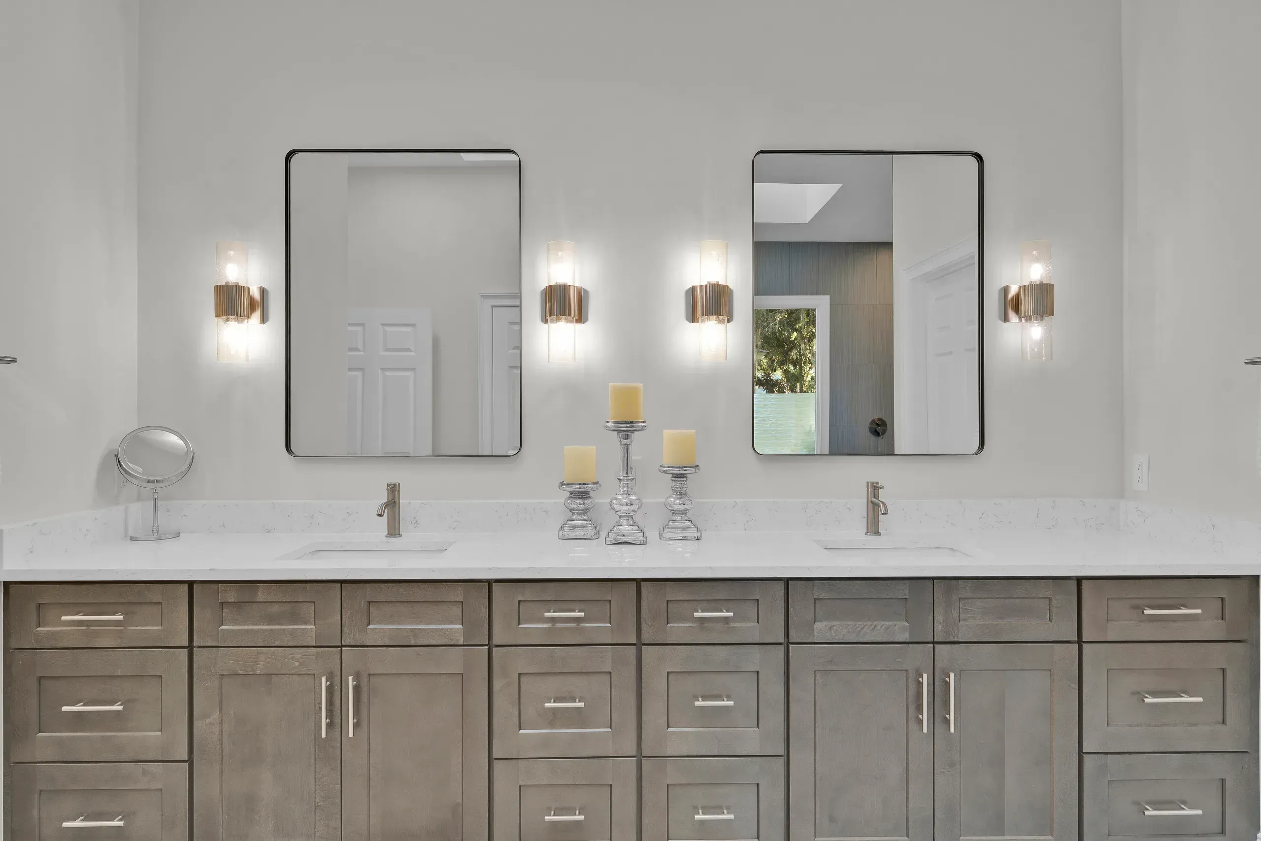 A double bathroom vanity with gray wood cabinetry, a white quartz countertop, two rectangular framed mirrors, and wall sconces flanking each mirror.