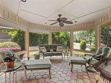 A screened porch addition features a beadboard ceiling with a fan, wicker and upholstered seating around a glass-top coffee table, and a tiled floor overlooking a wooded backyard.