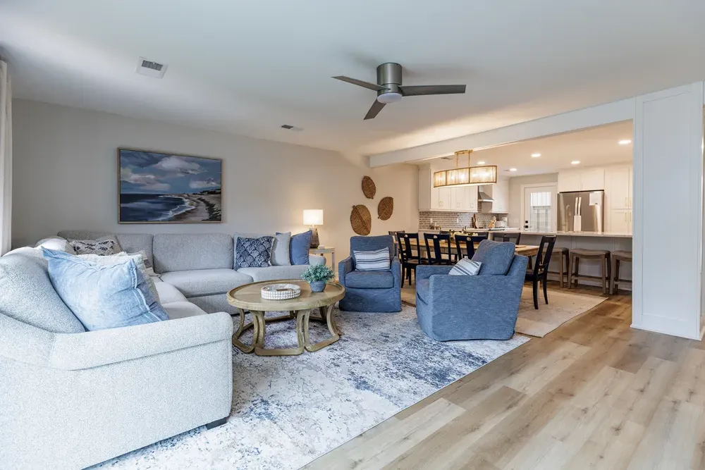 Open living room with gray sectional, blue armchairs, and view into kitchen and dining area