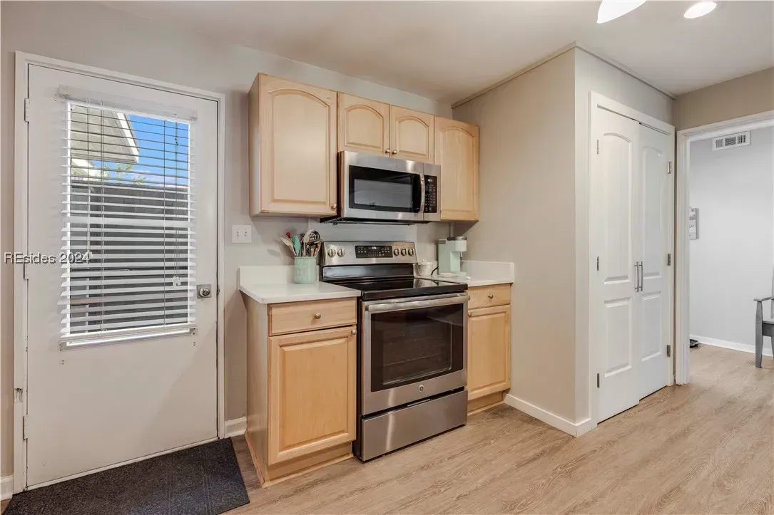 A kitchen with light wood cabinetry features a stainless steel range and microwave, a door leading outside, and light wood-look flooring.