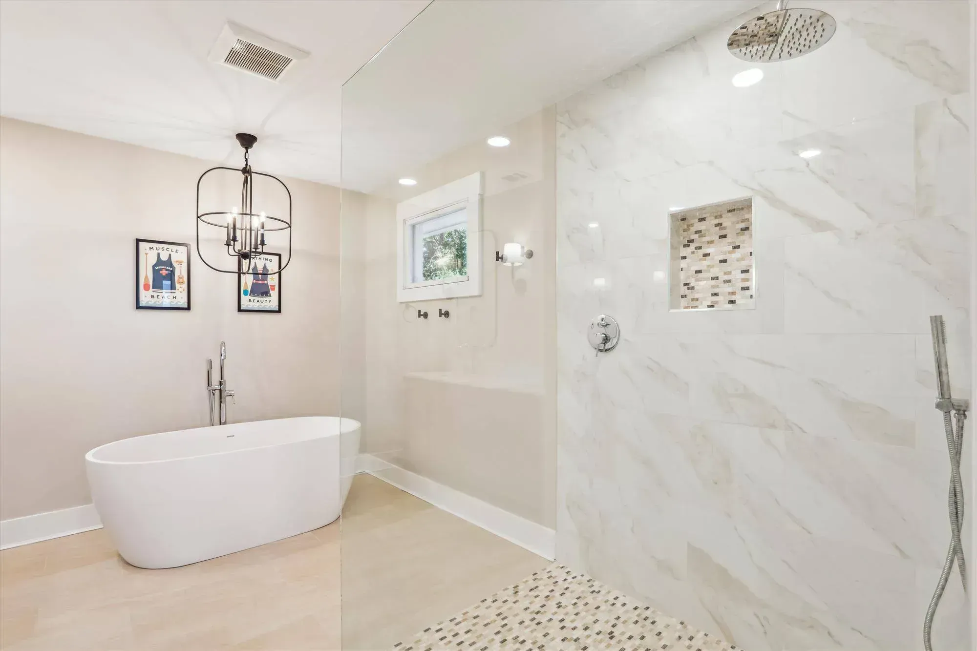 A remodeled bathroom features a freestanding oval soaking tub beneath a black chandelier, beside a glass-enclosed walk-in shower with marble-look tile and a tiled niche.