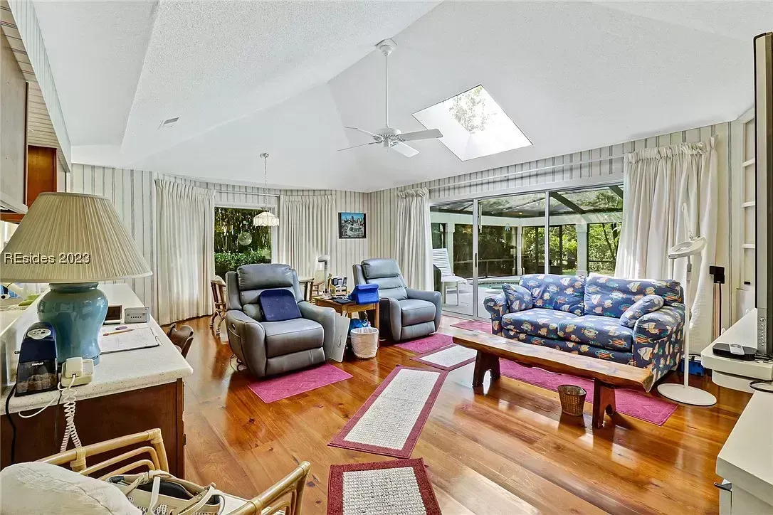 A living room with vaulted ceilings, a skylight, hardwood floors, and sliding glass doors leading to a screened porch beyond.