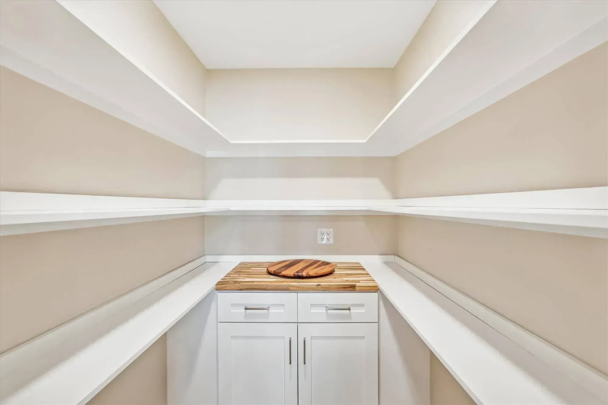 A walk-in pantry with white built-in shelving on both side walls and a butcher-block counter over white cabinetry at the back holding a round wooden lazy susan.