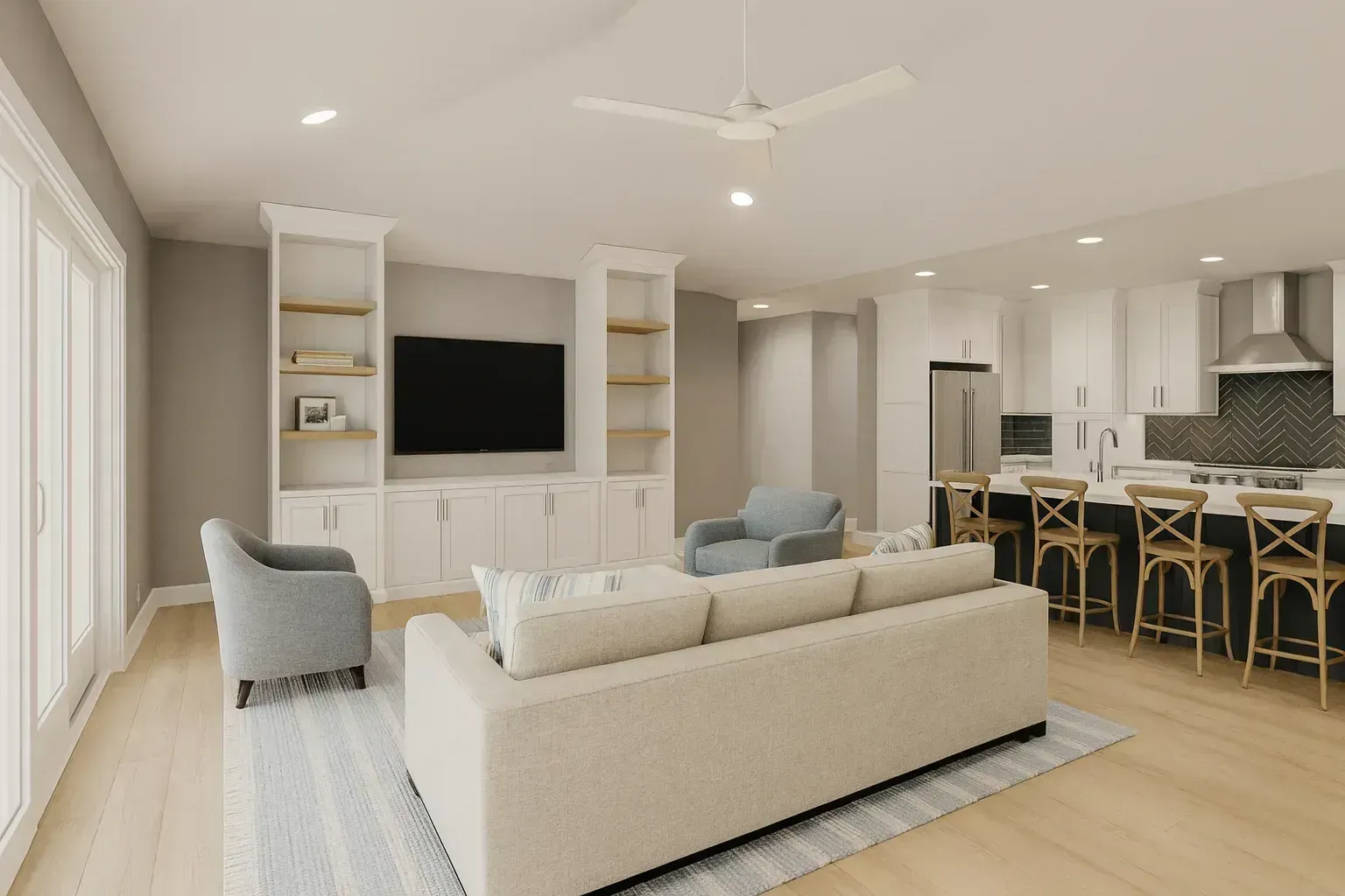 An open-concept living room with a beige sectional sofa, blue armchairs, and a built-in white entertainment center flows into a kitchen with white cabinetry, a dark green herringbone tile backsplash, and a navy island with wooden barstools.
